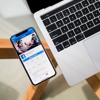 A phone on Facebook sits next to a computer on a glass table.