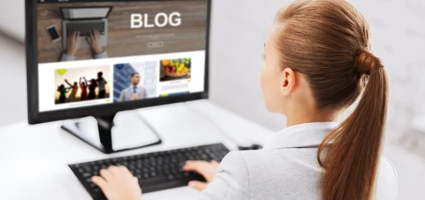 A woman with a ponytail sits at a desk viewing a blog website on a desktop screen, representing professional content creation for blogs with Jasper AI.