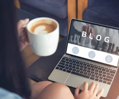 A person holding a cup of coffee while using a laptop, capturing the relaxed atmosphere of writing blogs with Jasper AI.