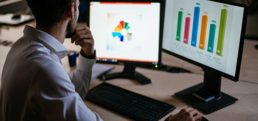 A businessman looking at recession proof marketing on two computer monitors.