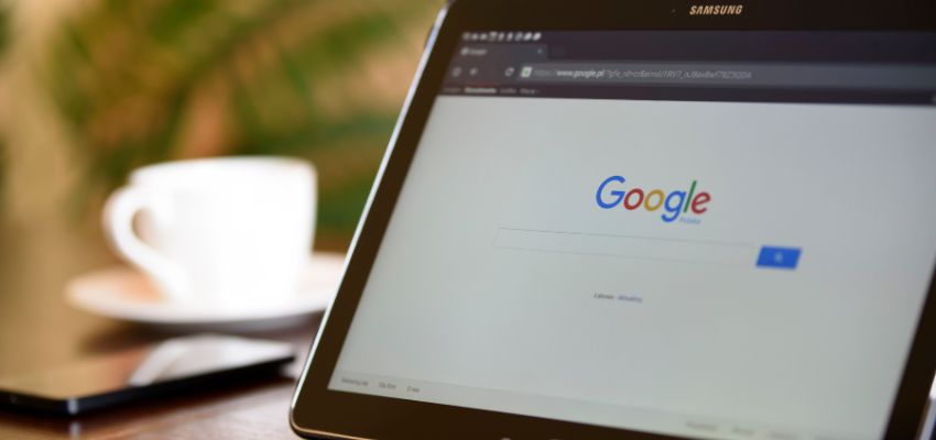 A tablet displaying the Google homepage next to a cup of coffee and smartphone, symbolizing digital tools and connectivity in the Google organizational structure.